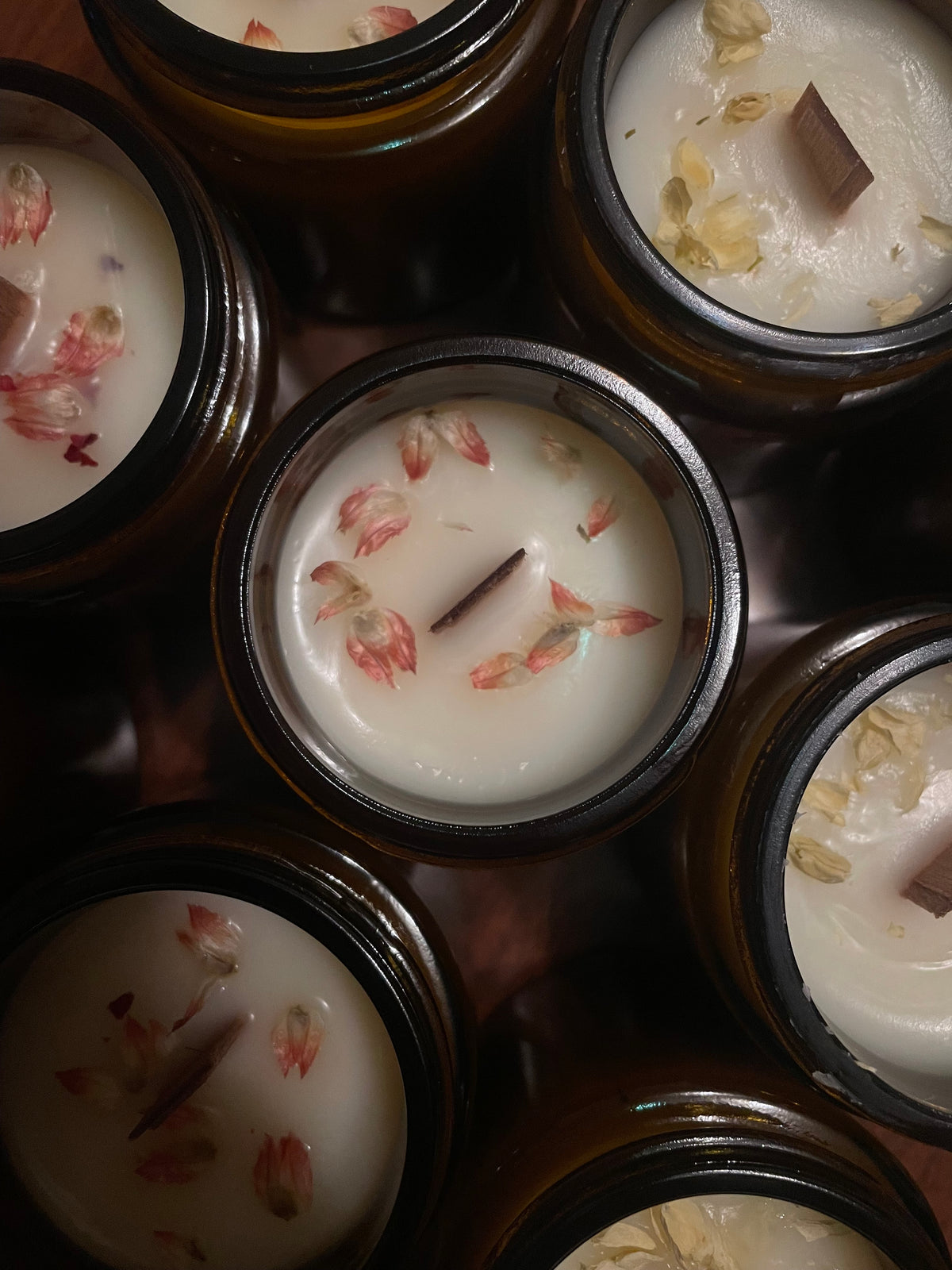 Candele in cera di soia in vasetti di vetro ambrato, con stoppino in legno e petali di fiori secchi, viste dall'alto